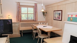 A cozy room with a wooden table, two chairs, a bench, a fireplace, a radiator, a window with curtains, a television, and a framed picture on the wall. - Cozy Apartment in Krimml (Krimml)