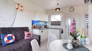 A compact living space with a sofa, a dining table, a kitchen area, and a small window. - Comfortable Holiday Homes With Terraces (Mielno)
