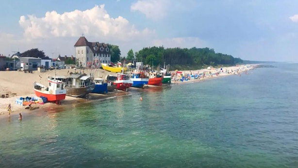 A beach with boats docked, a building with a red roof, and a sandy shore. - Comfortable Holiday Homes With Terraces (Mielno)
