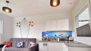 A compact living space with a grey sofa, a small kitchen with white cabinets, and a window with blinds. - Comfortable Holiday Homes With Terraces (Mielno)