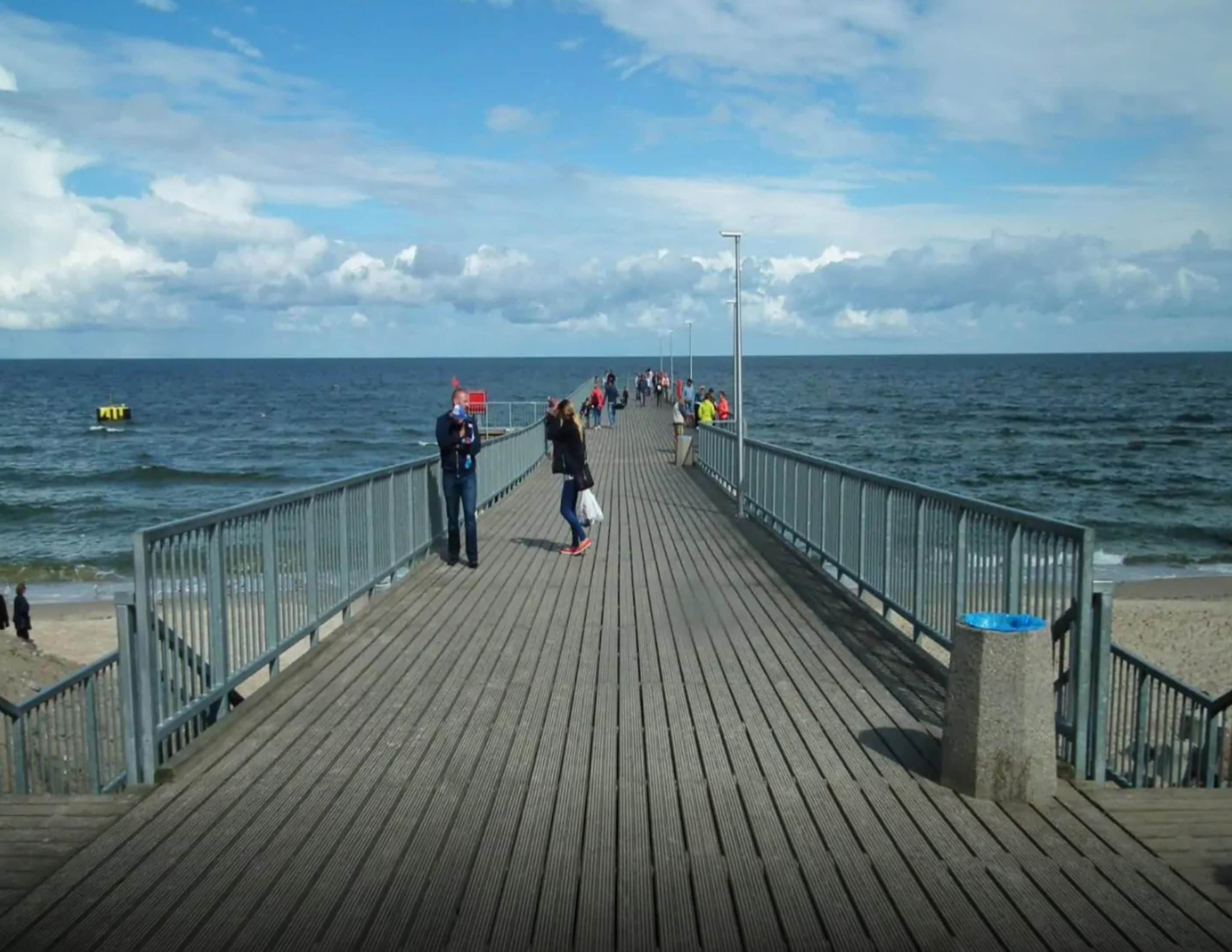 Un muelle de madera que se adentra en el mar, con gente caminando a lo largo de él.