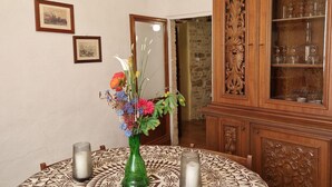Een eettafel met een tafelkleed met patroon, een groene vaas met bloemen en twee kaarsen.