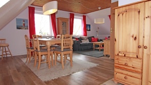 A cozy loft-style room with a dining area, a sofa, and a wardrobe. - Ferienwohnung im Ferienhaus Rosi, Fehmarn-schlagsdorf (Fehmarn)