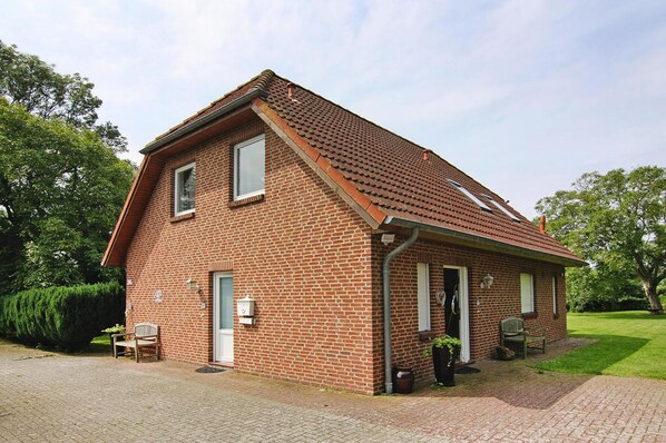 Une maison en briques avec un toit en pente, un porche à l’avant et un petit jardin.