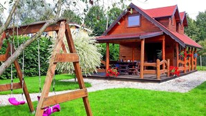 Une cabane en bois avec une véranda, une balançoire et une table de pique-nique, le tout situé dans une cour verdoyante.