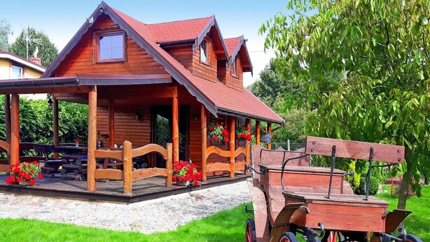 Une cabane en bois avec une véranda, un chariot en bois et un jardin parsemé de fleurs rouges.