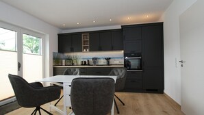 A modern kitchen with dark cabinets, a white countertop, and a dining area with a white table and two chairs. - Ferienhaus am Rande der Lewitz (Lüblow)