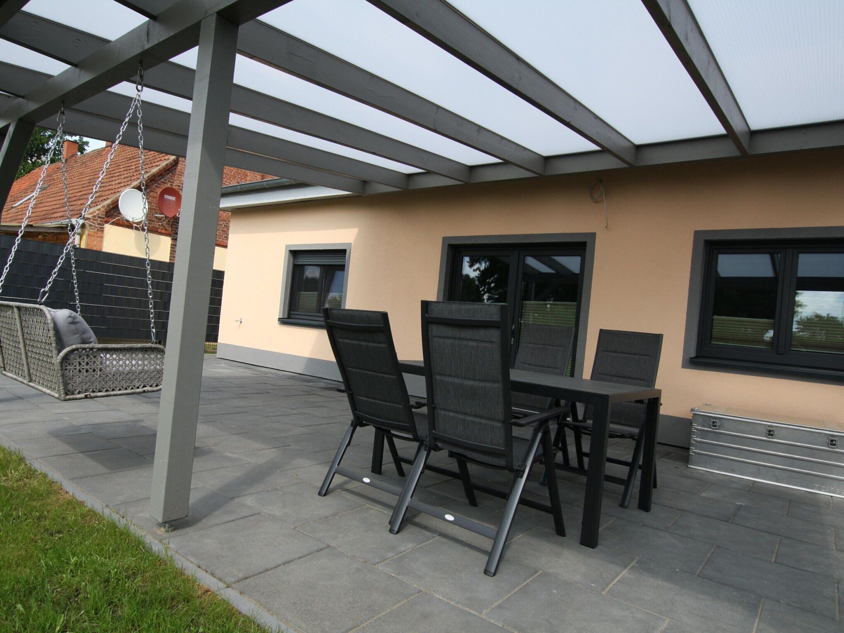 An outdoor patio with a pergola, a swing set, and a table with chairs.