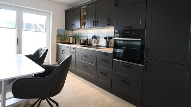 A modern kitchen with dark cabinets, a white countertop, and a built-in oven. - Ferienhaus am Rande der Lewitz (Lüblow)