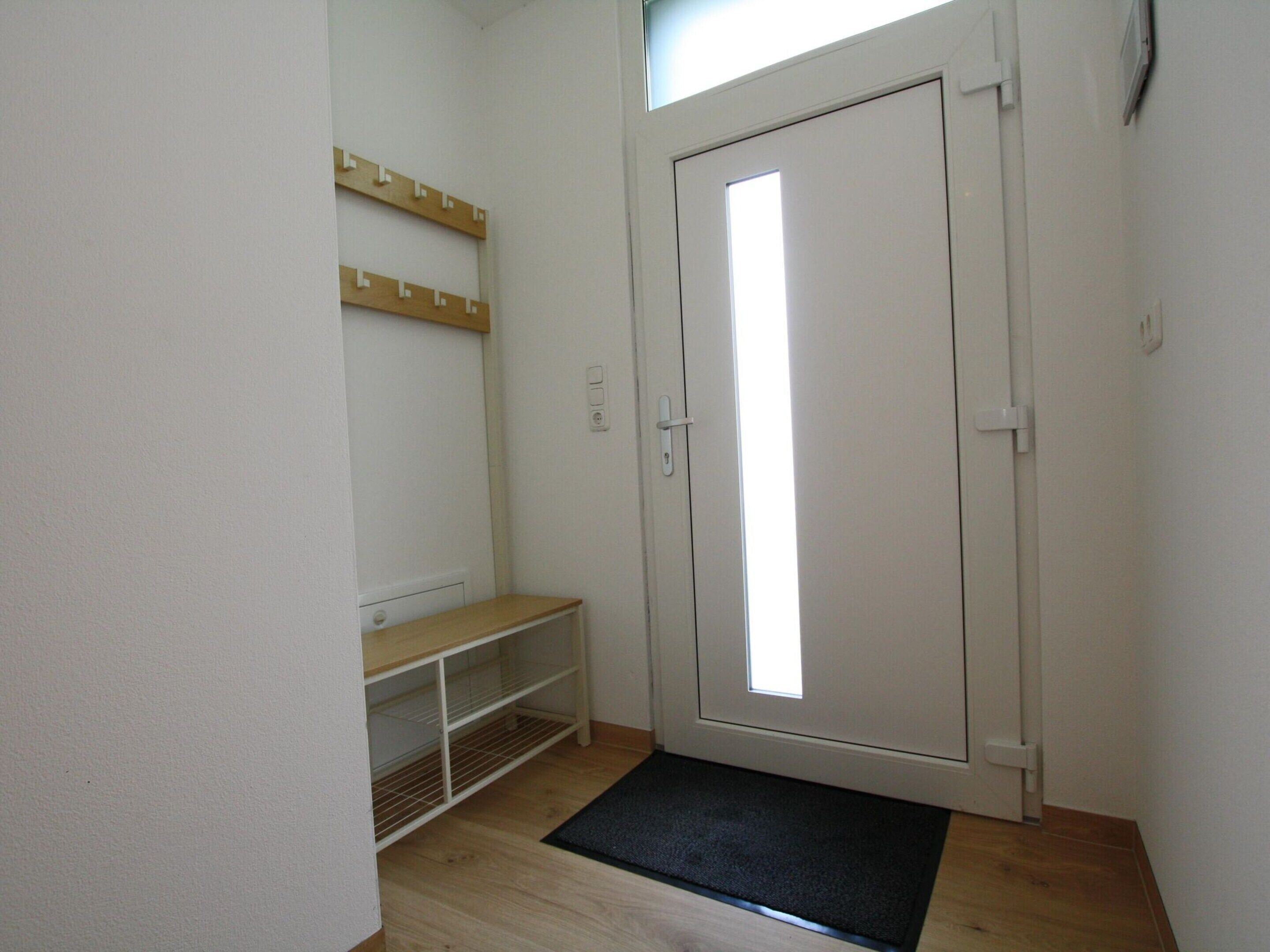 A small, clean room with a white door, a wooden bench, and a shelf above the bench.