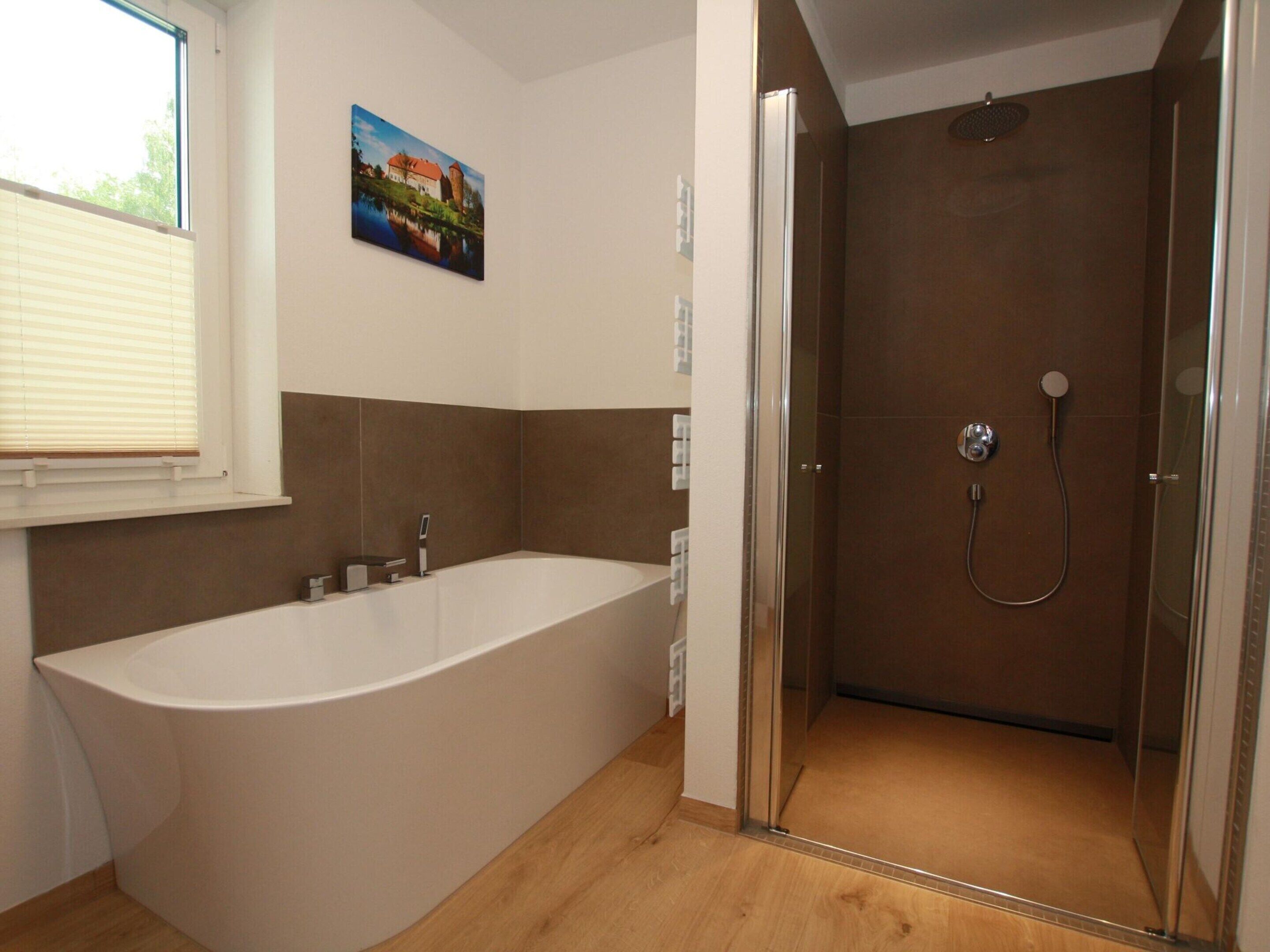 A modern bathroom with a freestanding bathtub, a glass-enclosed shower, and a window with blinds.