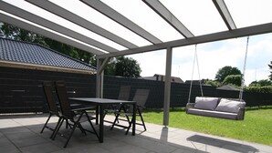 A covered patio area with a table and chairs, a swing, and a fenced backyard. - Ferienhaus am Rande der Lewitz (Lüblow)
