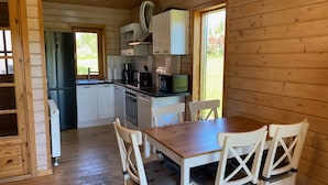 Une cuisine compacte avec des meubles blancs, un réfrigérateur en acier inoxydable, un four à micro-ondes et une machine à café. On y trouve une table à manger en bois avec quatre chaises.
