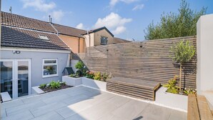 A residential backyard with a tiled patio, a wooden fence, and various plants. - 2 bedroom accommodation in Treorchy (Treorchy)