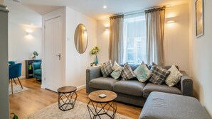 A modern living room with a grey sofa, two round tables, a mirror, and a window with curtains. - 2 bedroom accommodation in Treorchy (Treorchy)