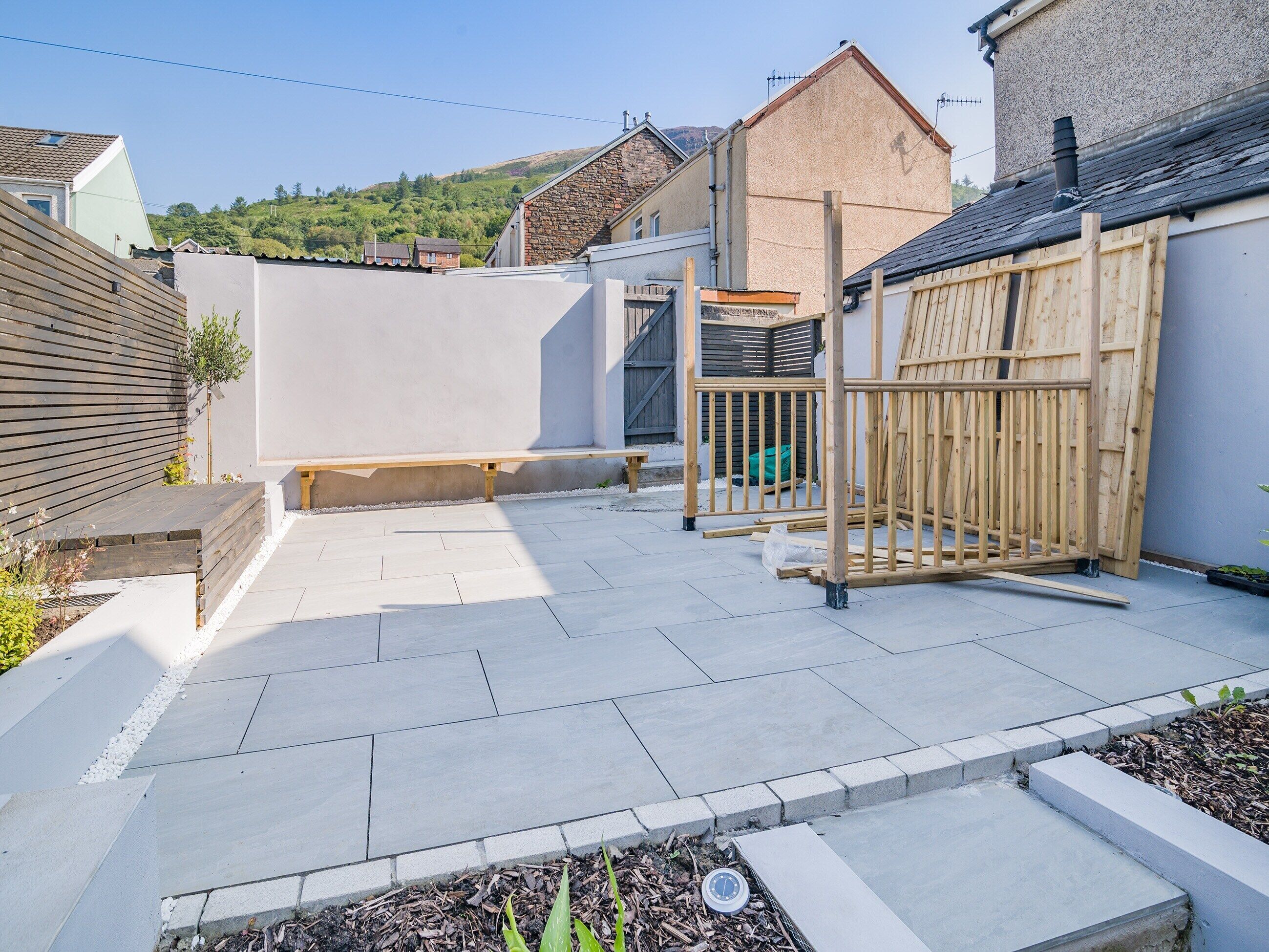 A residential backyard with a patio, a wooden fence, and a stone wall.