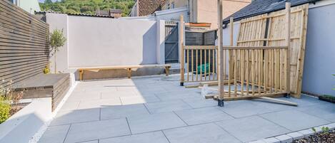 A residential backyard with a patio, a wooden fence, and a stone wall.