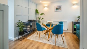 A modern living room with a dining area, featuring a glass table, blue chairs, a black cabinet, and a potted plant. - 2 bedroom accommodation in Treorchy (Treorchy)