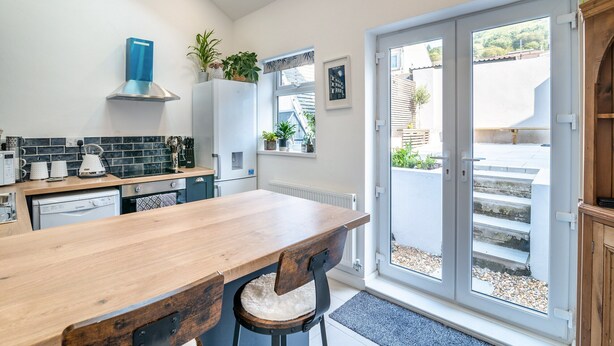 A modern kitchen with a wooden table and chairs, a built-in oven, and a large window with a view of the outside. - 2 bedroom accommodation in Treorchy (Treorchy)