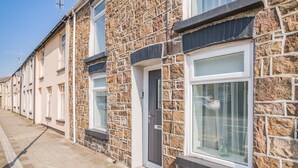 A row of terraced houses with stone facades, white-framed windows, and a paved sidewalk. - 2 bedroom accommodation in Treorchy (Treorchy)