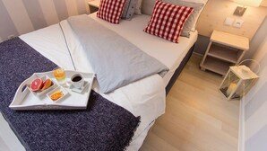 A neatly made bed with striped bedding, a tray with fruit and coffee, and bedside tables with lamps. - Comfortable Apartment in Miedzyzdroje (Miedzyzdroje)