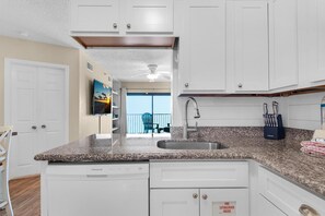 A kitchen with white cabinets, a granite countertop, a dishwasher, and a fire extinguisher sign. - Sundunes 162 (Navarre)