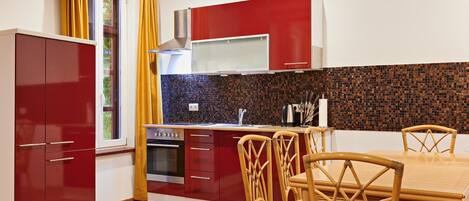 A modern kitchen with red cabinets, a tiled backsplash, and a dining area with wicker chairs and a wooden table.