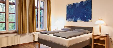 Un dormitorio con cama, mesita de noche, lámpara, ventana con cortinas, radiador y alfombra.