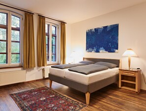 Une chambre à coucher comprenant un lit, une table de chevet, une lampe, une fenêtre avec des rideaux, un radiateur et un tapis.