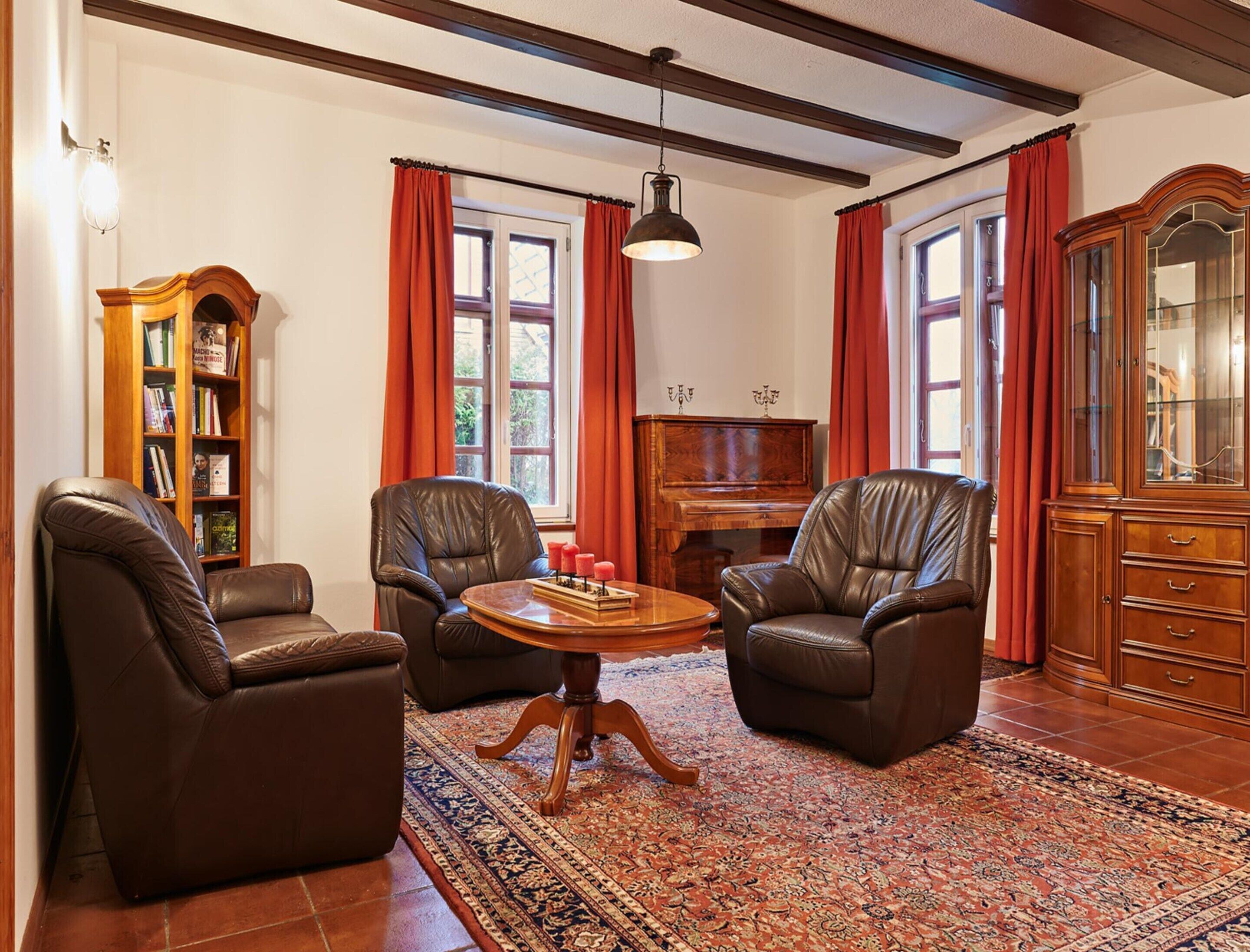 A room with two leather armchairs, a wooden coffee table, a piano, a bookshelf, and a cabinet.