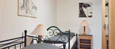 A bedroom with a bed, two bedside tables with lamps, a wooden wardrobe, and two wall-mounted artworks.