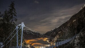 A suspension bridge over a valley with snow-covered mountains and a lit-up town below. - Terraced Houses Oliver, Langenfeld (Laengenfeld)