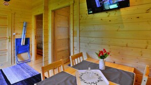 L’intérieur d’un chalet en bois, avec une table à manger dressée pour deux personnes, un téléviseur fixé au mur et une horloge également accrochée au mur.
