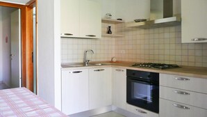 Una cucina compatta con mobili bianchi, un fornello a gas, un forno e un lavello.