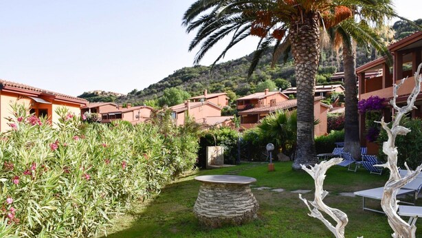 Un cortile con un tavolo in pietra, poltrone relax e una palma.