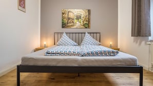 Une chambre à coucher avec un lit, deux tables de chevet, un tableau au mur et une fenêtre avec des rideaux.