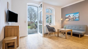 Un salon moderne avec un plancher en bois, un canapé gris, une table en bois, un fauteuil gris et un téléviseur posé sur un meuble en bois.