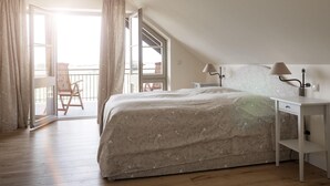 Ein Schlafzimmer mit Bett, Nachttisch, Lampe, Stuhl und einem Balkon mit Aussicht.