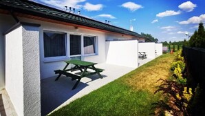 Et moderne hus med terrasse, et grønt picnicbord og en lille have.