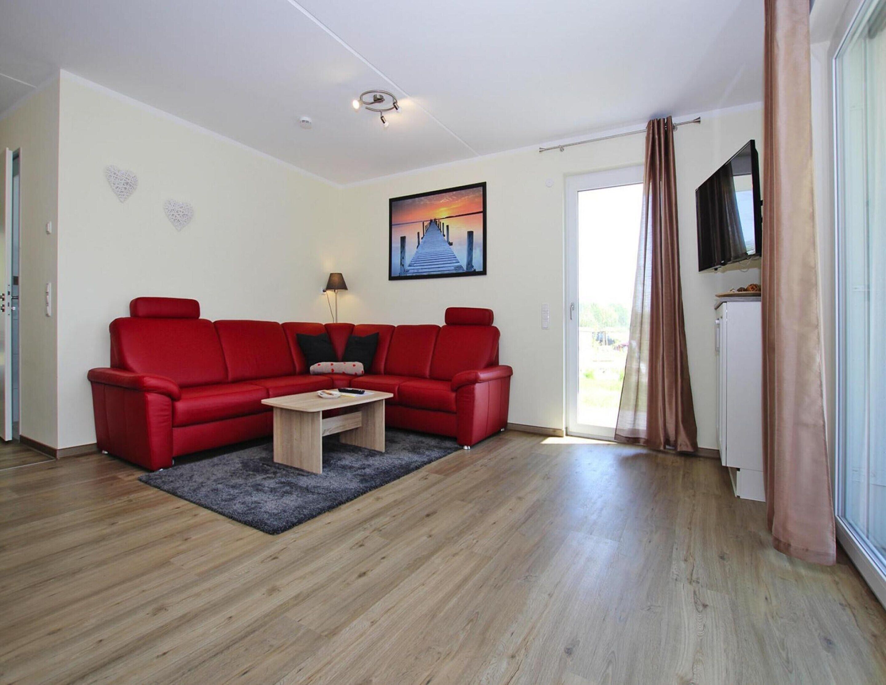 A modern living room with a red sofa, a wooden coffee table, and a painting of a sunset.