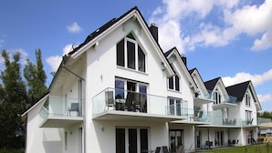 A modern two-story house with a balcony, large windows, and a well-maintained lawn. - Appartement Hafenflair am Plauer See (Plau am See)