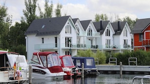 A row of white houses with dark roofs, a dock with boats, and a calm water body. - Appartement Hafenflair am Plauer See (Plau am See)