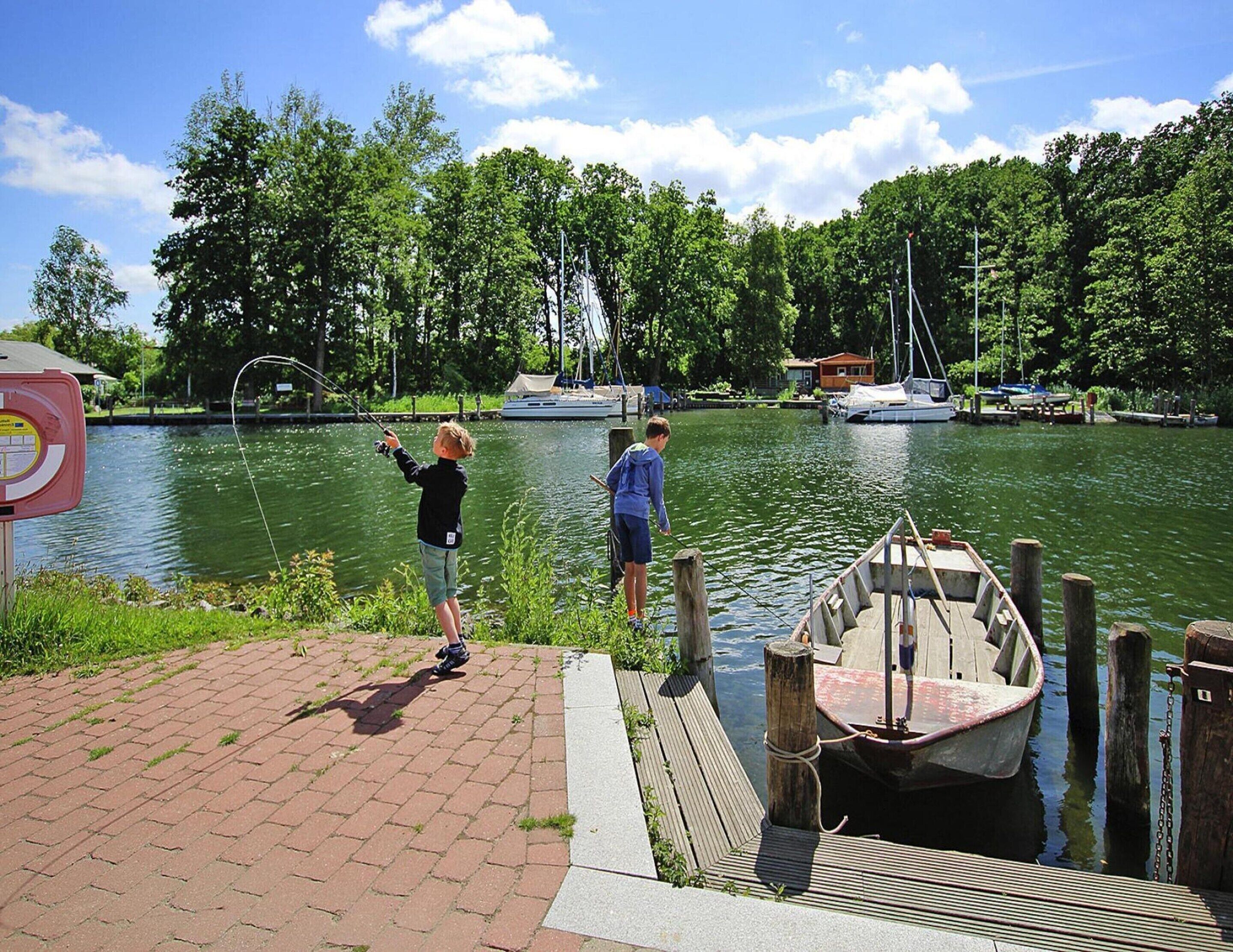 A dock with a small boat, a paved walkway, and a calm water body with boats in the background.