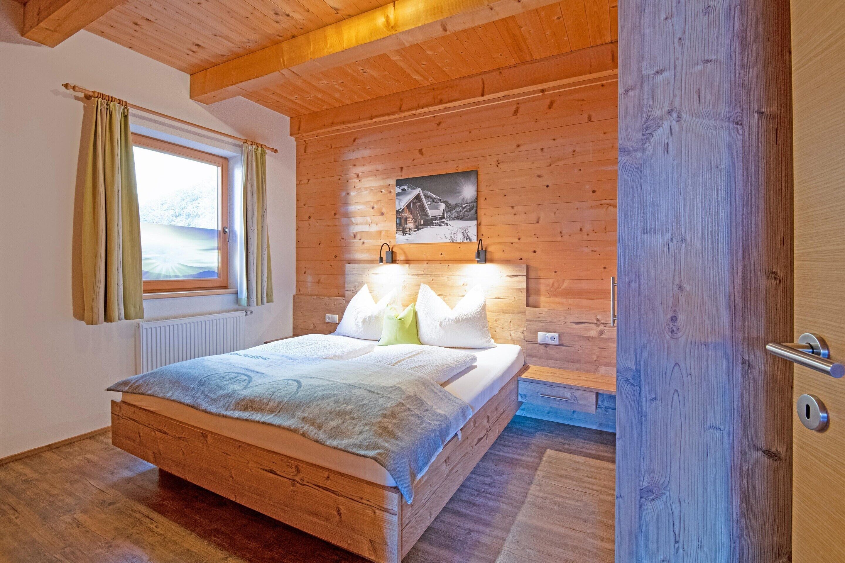 A wooden-paneled bedroom with a bed, a window with curtains, a radiator, and a painting on the wall.