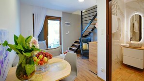 Ein Essbereich mit Tisch für zwei Personen, einer Blumenvase und Blick auf eine Treppe, die zu einem Badezimmer führt.