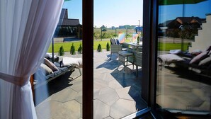 Eine moderne Außenpatio mit sechseckigen Fliesen, einer Sitzecke mit Kissen und Blick auf ein Sportfeld und Gebäude.