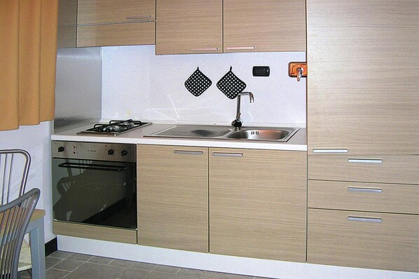 Une cuisine avec des meubles de rangement en bois, une cuisinière, un évier et deux torchons noirs accrochés au mur.