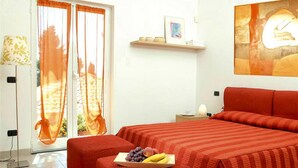 A bedroom with a red-striped bedspread, a fruit tray on the bedside table, and a view through a glass door. - Residence Villa Beuca, Cogoleto (Cogoleto)