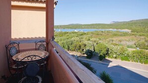 A balcony with a tiled table and chairs, overlooking a coastal landscape with greenery and a body of water. - Golfo Aranci Stay at Baia de Bahas (Golfo Aranci)