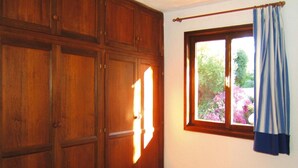A bedroom with a bed, wooden wardrobe, and a window with curtains. - Golfo Aranci Stay at Baia de Bahas (Golfo Aranci)
